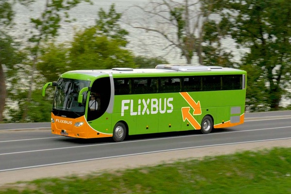 Der grün-orangefarbene Flixbus fährt auf der öffentlichen Straße entlang eines Sees.